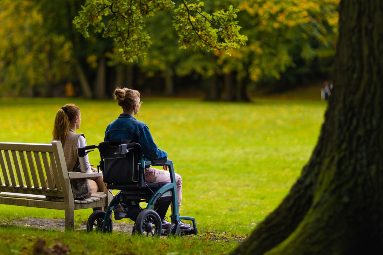Two women enjoy relaxation in a summer park with accessible seating.