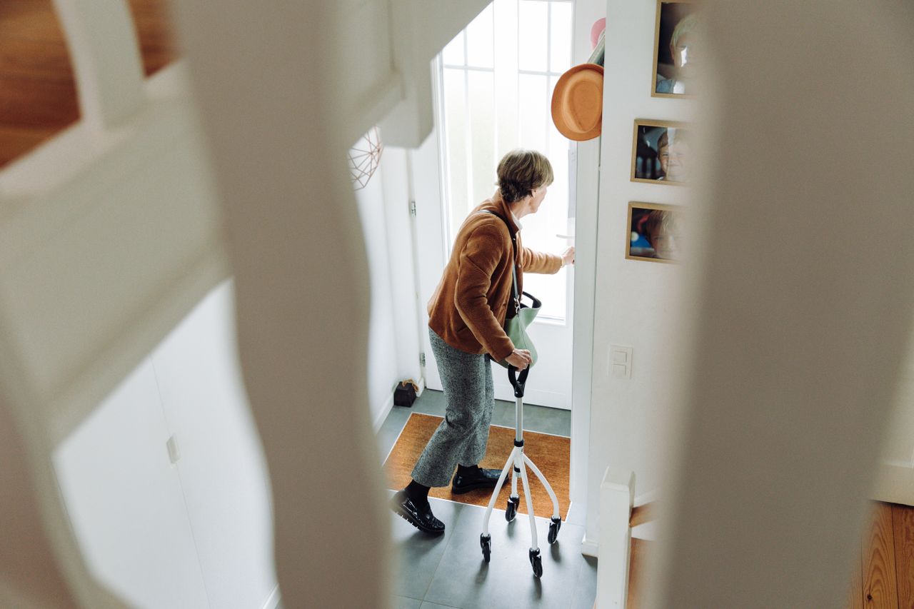 about-details Senior woman using rollator indoors near doorway, preparing to leave home.